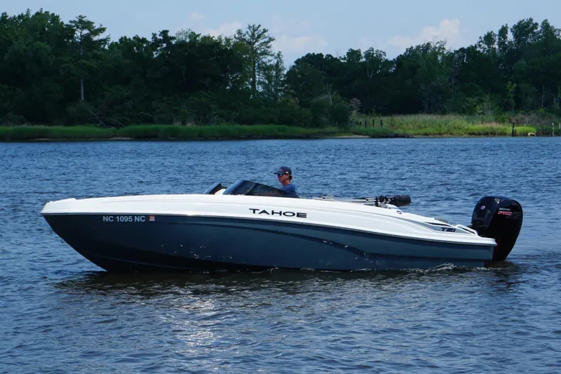 Slide: The Image of 2024 Tahoe T21 boat cruising on a serene lake with lush green shoreline. - 15
