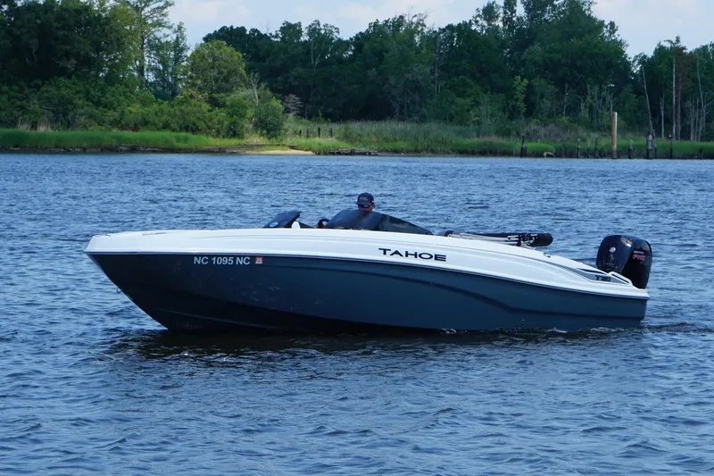 Slide: The Image of 2024 Tahoe T21 boat cruising on a serene lake with lush green shoreline. - 4