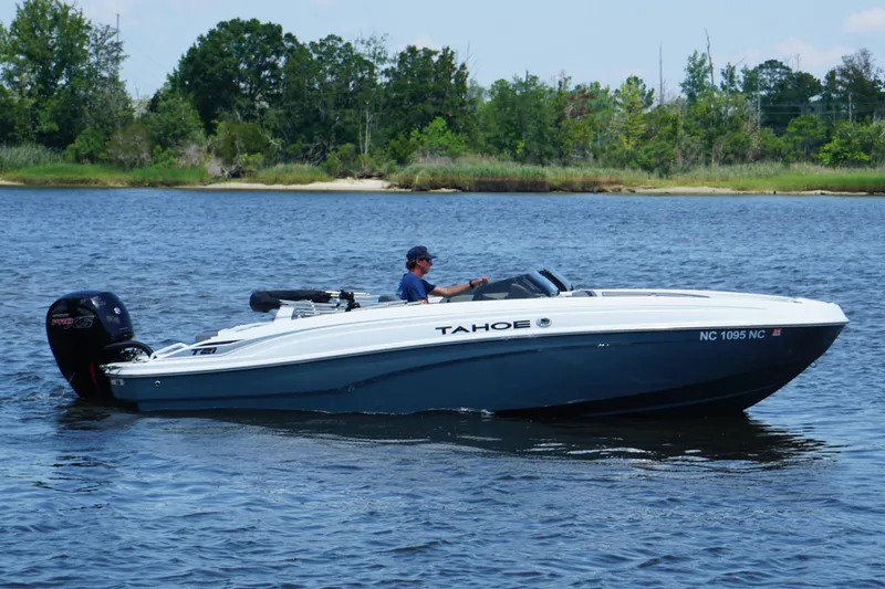 Slide: The Image of 2024 Tahoe T21 boat cruising on a serene lake with lush greenery in the background. - 1