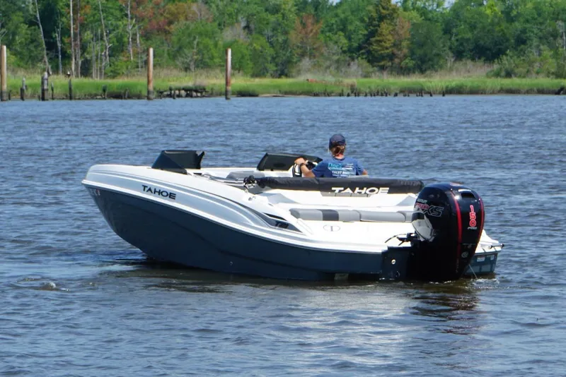 Slide: The Image of 2024 Tahoe T21 boat cruising on a calm lake with lush green shoreline. - 20