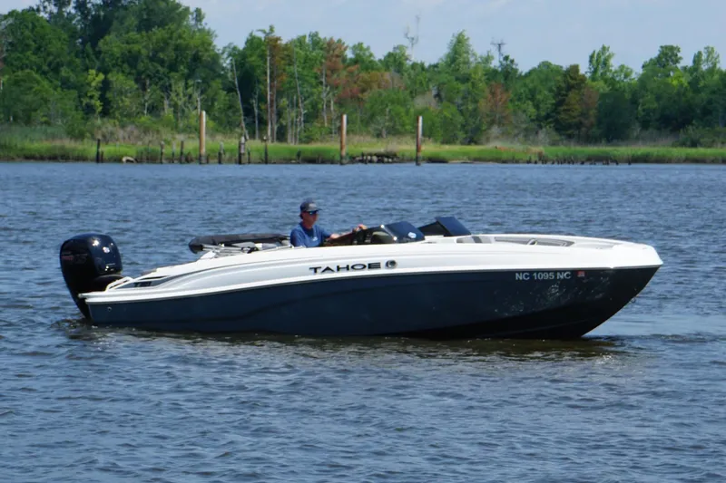 Slide: The Image of 2024 Tahoe T21 boat cruising on a calm lake with lush green shoreline. - 17