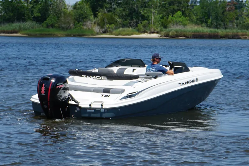 Slide: The Image of 2024 Tahoe T21 boat cruising on a serene lake with lush greenery in the background. - 19