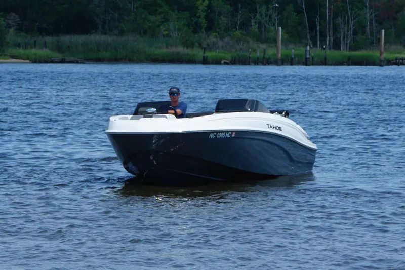 Slide: The Image of 2024 Tahoe T21 boat cruising on a calm lake with lush green shoreline. - 18