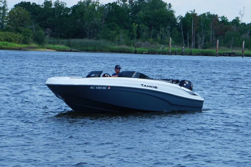 Slide: The Image of 2024 Tahoe T21 boat cruising on a serene lake with lush green shoreline. - 23