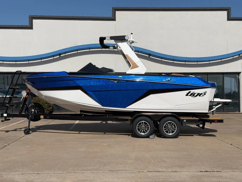 The Image of A blue and white 2027 Tigé Z1 boat on a trailer in front of a modern building. - 1