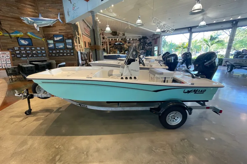 Slide: The Image of 2026 Mako Pro Skiff 15 CC boat displayed in a showroom with marine decor. - 1