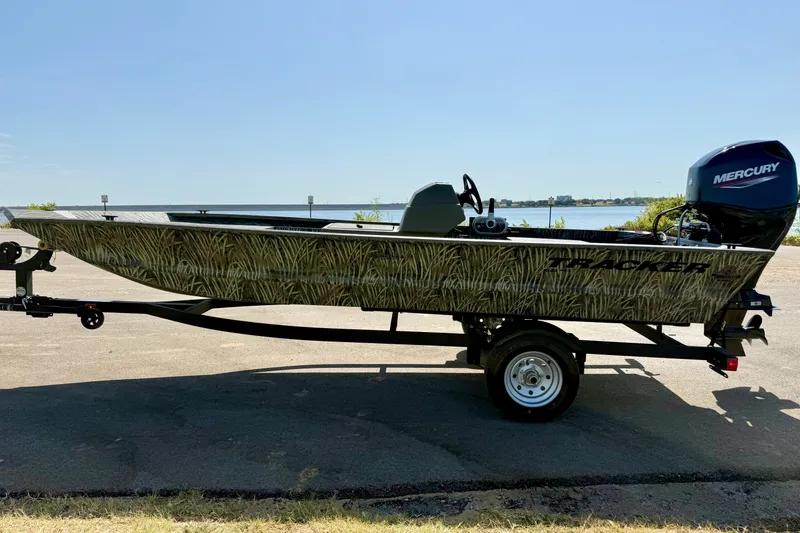 Slide: The Image of 2026 Tracker Grizzly 1648 SC boat with camouflage design on a trailer by the water. - 13