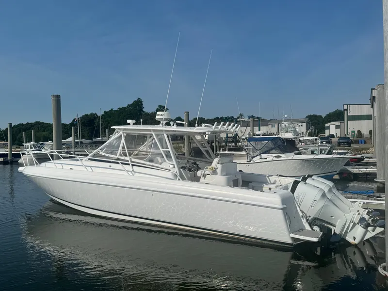 Slide: The Image of A 2002 Intrepid 377 Walkaround docked in a calm marina. The boat features a sleek, white design. - 2