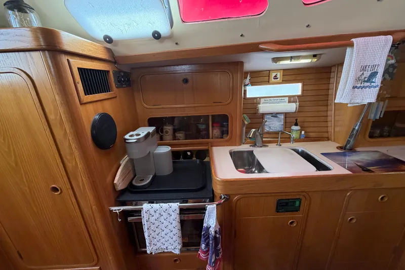 Slide: The Image of Cozy kitchen area in a 1988 Beneteau Oceanis 390 sailboat, featuring wooden cabinetry and modern appliances. - 21