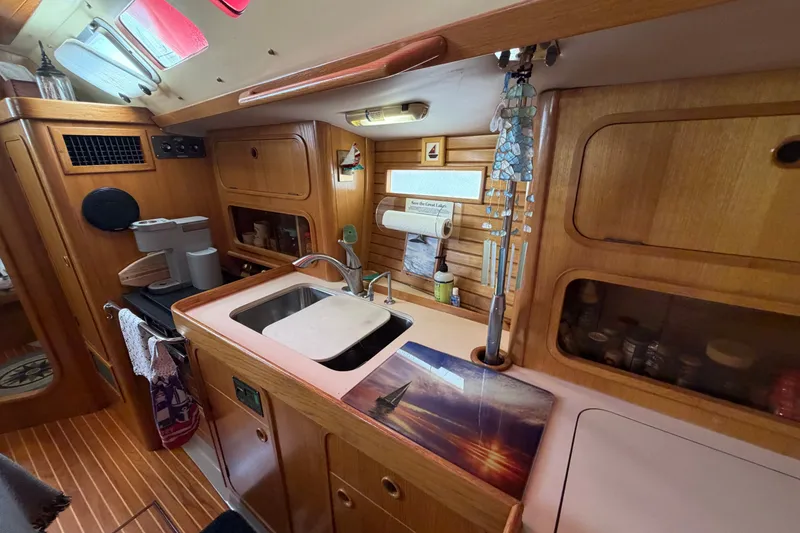 Slide: The Image of Cozy kitchen area in a 1988 Beneteau Oceanis 390 sailboat, featuring wooden cabinetry and a sink. - 22