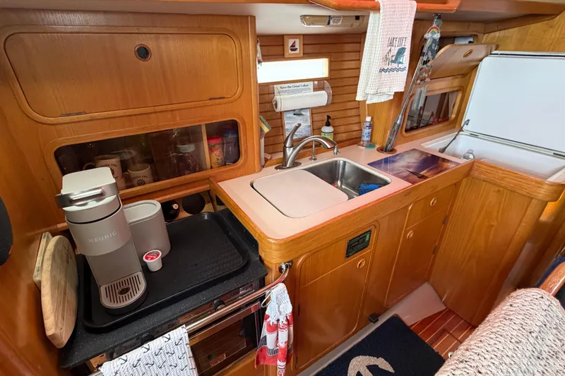 Slide: The Image of Galley of 1988 Beneteau Oceanis 390 sailboat with wooden cabinetry and modern appliances. - 24