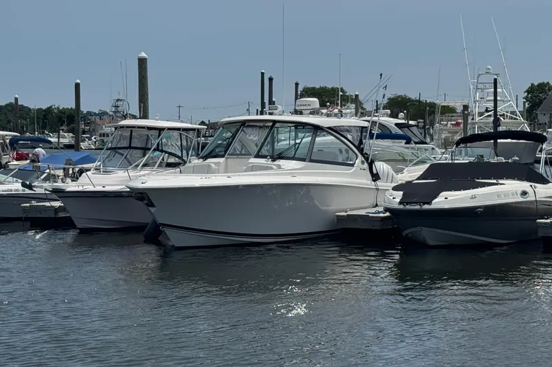 The Image of 2025 Pursuit DC 306 Dual Console boat docked at marina, surrounded by other vessels. - 0