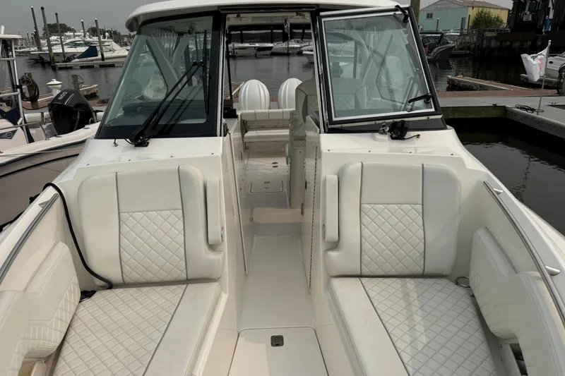 Slide: The Image of 2025 Pursuit DC 306 Dual Console boat interior with white quilted seating at a marina. - 33