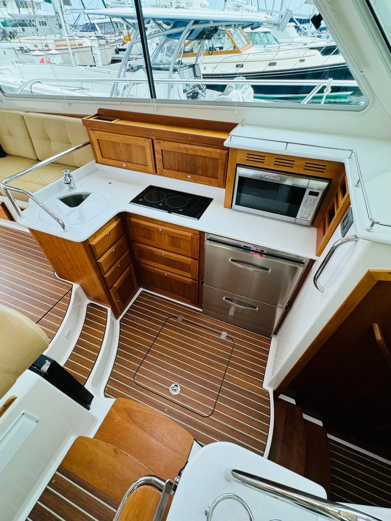 Slide: The Image of The galley of a 2018 Back Cove 37 with wooden cabinets, sink, stove, and microwave. - 41
