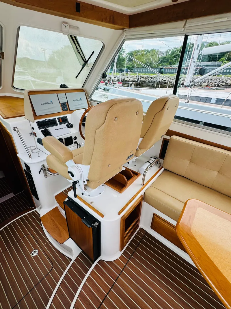 Slide: The Image of Interior of a 2018 Back Cove 37 with two beige seats and a wooden table. - 49