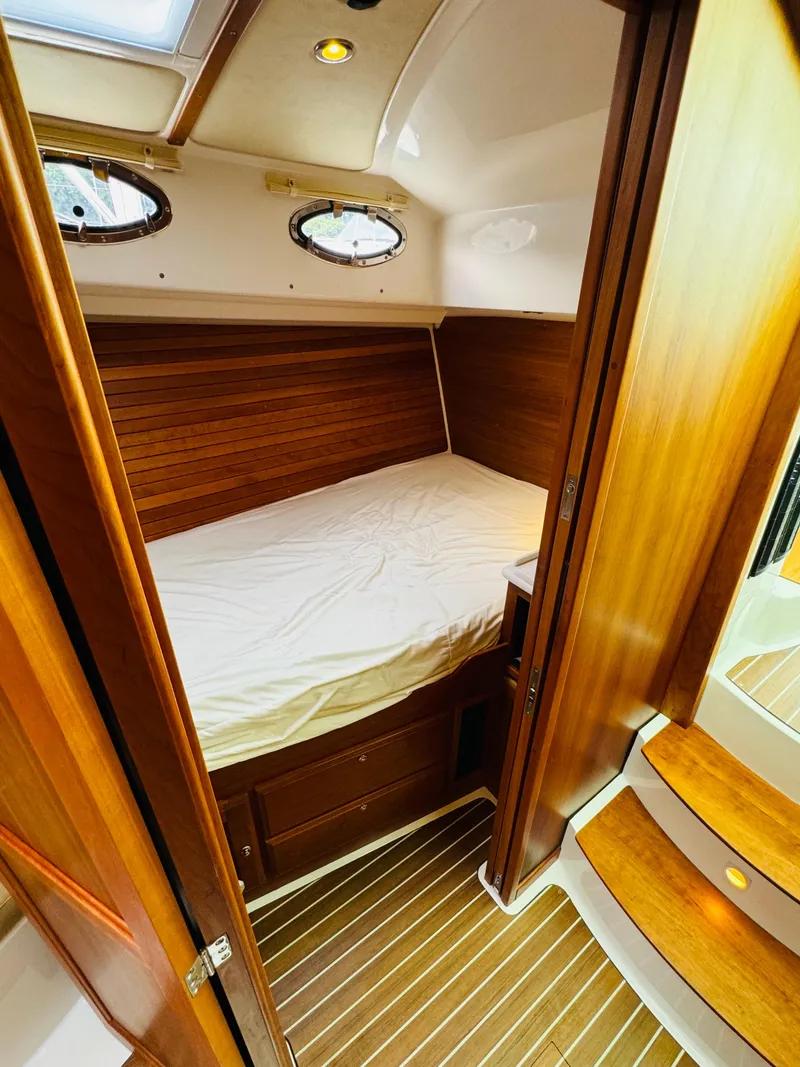 Slide: The Image of The cabin of the 2018 Back Cove 37 features a cozy bed with wood paneling and portholes. - 39