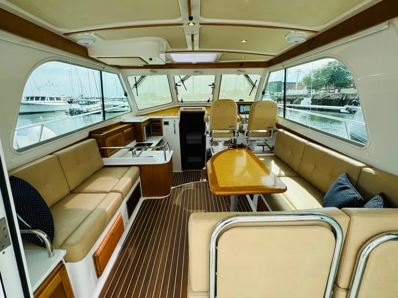 Slide: The Image of Interior of a 2018 Back Cove 37 with beige seating and wooden table, overlooking a marina. - 24