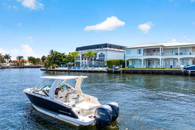 Slide: The Image of 2023 Chaparral 280 OSX boat cruising near waterfront homes under a clear blue sky. - 3