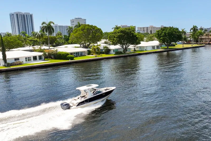 Slide: The Image of 2023 Chaparral 280 OSX cruising on a scenic waterfront with modern homes and palm trees. - 10