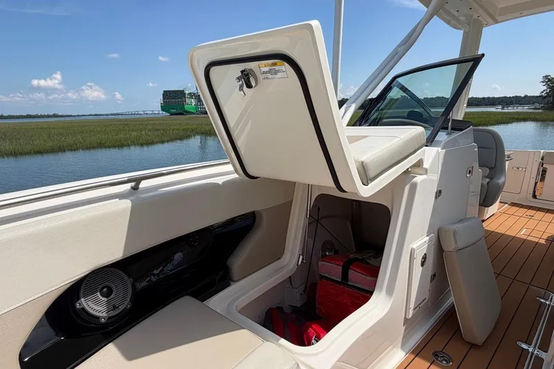 Slide: The Image of 2022 Boston Whaler 240 Vantage boat interior with open storage compartment, docked by scenic waterway. - 11