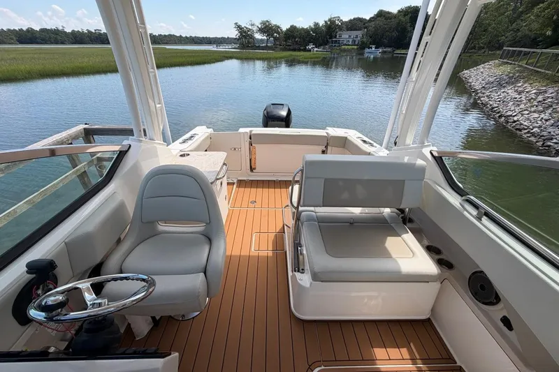 Slide: The Image of 2022 Boston Whaler 240 Vantage boat interior with seating and steering wheel, docked by a scenic lake. - 20