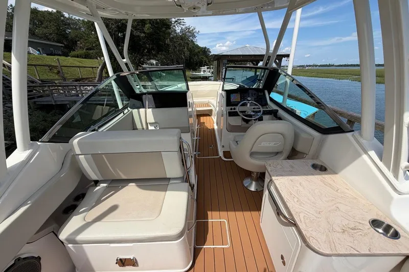 Slide: The Image of 2022 Boston Whaler 240 Vantage boat interior with seating and helm, docked by a scenic river. - 13