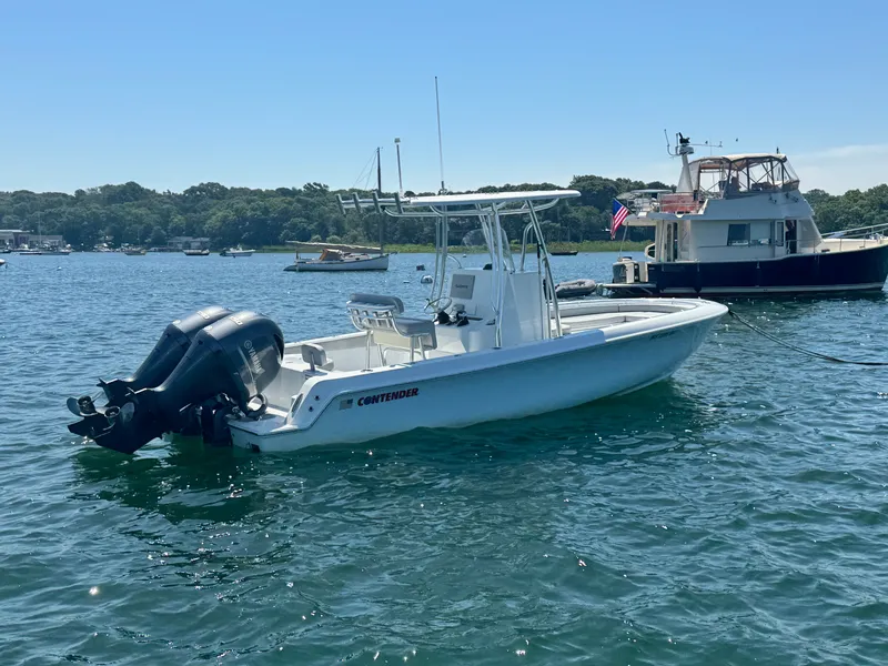 Slide: The Image of A 2024 Contender 24 Sport boat on calm water, featuring twin outboard engines and a T-top. - 5
