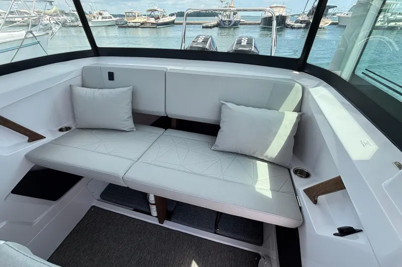 Slide: The Image of 2025 Axopar 29 XC Cross Cabin interior with cushioned seating, docked boats visible outside. - 20