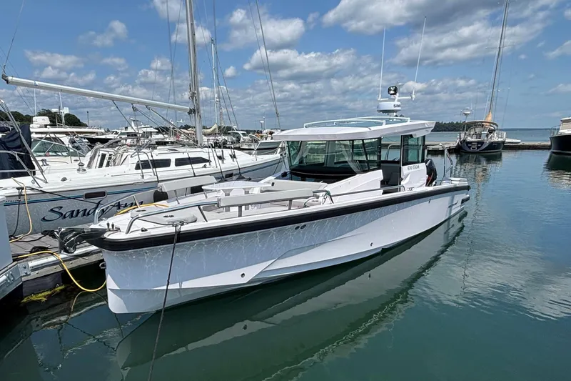 Slide: The Image of 2025 Axopar 29 XC Cross Cabin boat docked in a marina under a cloudy sky. - 0