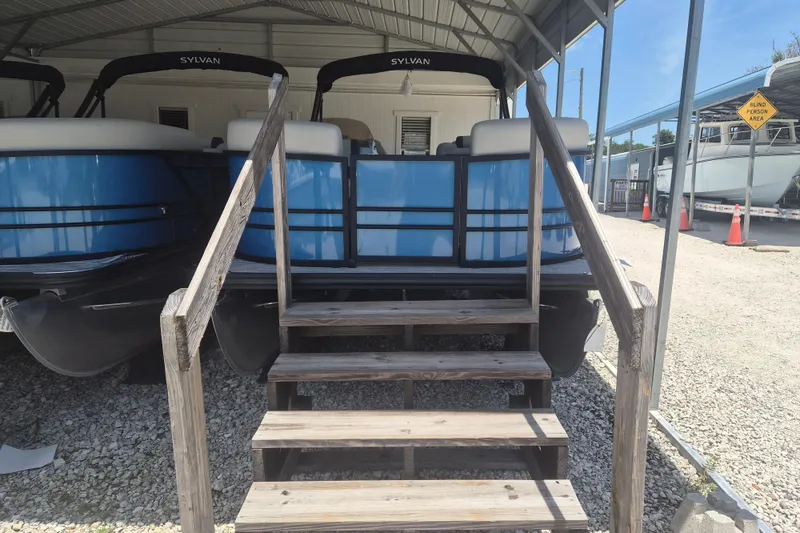 The Image of 2026 Sylvan Mirage Fish 820 Party Fish pontoon boat under shelter with wooden steps. - 1