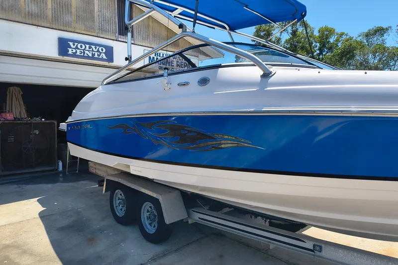 Slide: The Image of 2009 Regal 2400 Bowrider boat on trailer, blue and white design, parked near marine repair shop. - 1