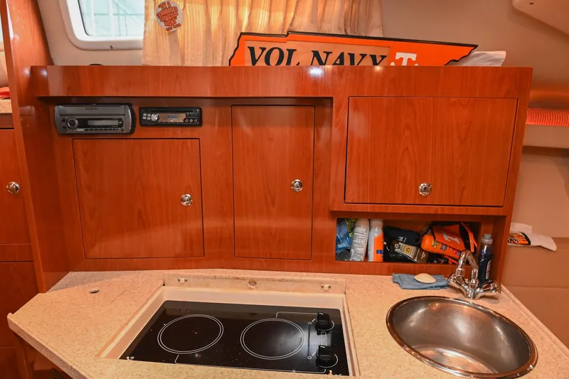 Slide: The Image of 2009 Regal 3060 Window Express boat interior with kitchenette, featuring stove, sink, and wooden cabinetry. - 35