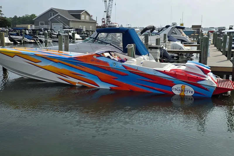 The Image of 2003 Cigarette 38' Top Gun speedboat with vibrant graphics docked at a marina. - 0