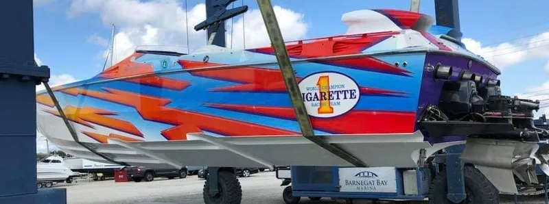 Slide: The Image of A 2003 Cigarette 38' Top Gun boat with a striking, colorful design being lifted on land. - 13