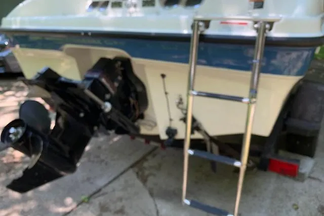 Slide: The Image of 2011 Bayliner 185 Bowrider boat with ladder and outboard motor, parked on concrete. - 2