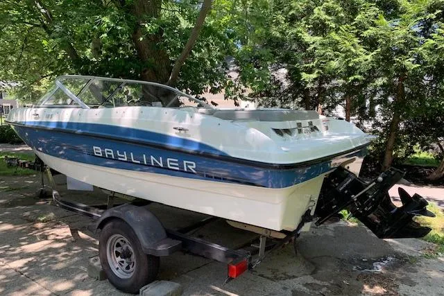 The Image of 2011 Bayliner 185 Bowrider on trailer, parked outdoors under trees. - 1