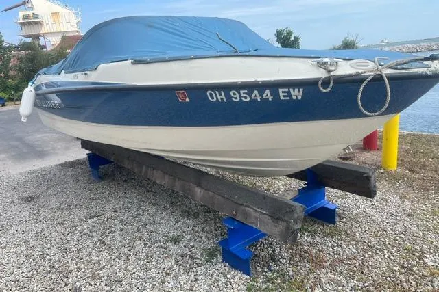 Slide: The Image of 2011 Bayliner 185 Bowrider boat with blue cover on a stand by the water. - 3