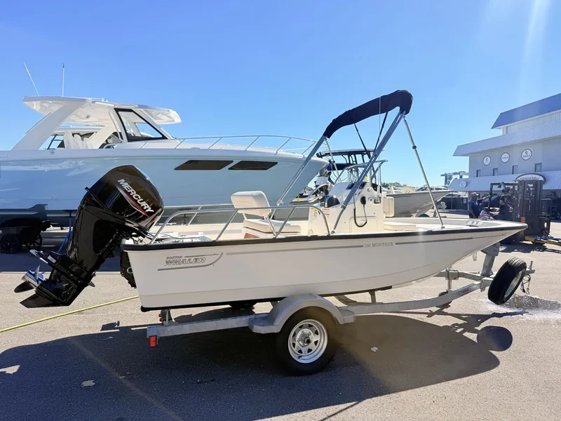 Slide: The Image of A 2027 Boston Whaler 150 Montauk on a trailer, parked next to a larger boat. - 3