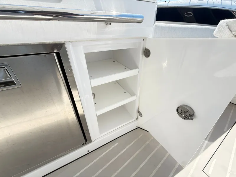 Slide: The Image of An open white cabinet with two shelves next to a stainless steel appliance on a boat. - 11