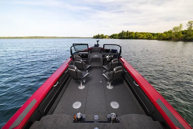 Slide: The Image of The image shows a Lund 2275 Tyee Sport boat on a calm lake with a wooded shoreline. - 2