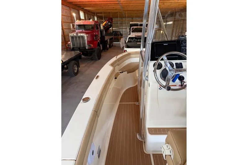 Slide: The Image of 2019 Scout 215 XSF boat interior with steering wheel, parked in a garage with trucks. - 8