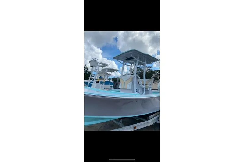 Slide: The Image of 2026 Exuma 22 boat with T-top, light blue and white design, on trailer under cloudy sky. - 7