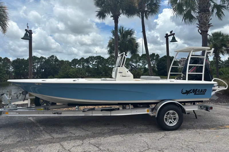 Slide: The Image of 2026 Mako 18 Pro Skiff boat on trailer, parked near palm trees under cloudy sky. - 1