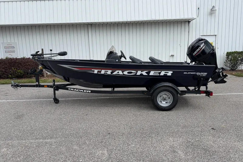The Image of 2026 Tracker Super Guide V-16 SC fishing boat on trailer, parked outdoors. - 0