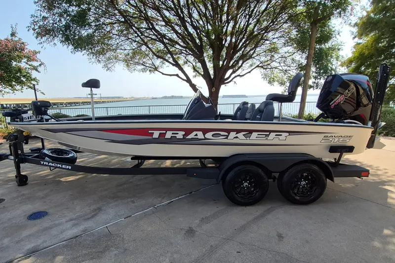 The Image of 2026 Tracker Savage 215 boat on trailer by waterfront, under tree shade. - 0