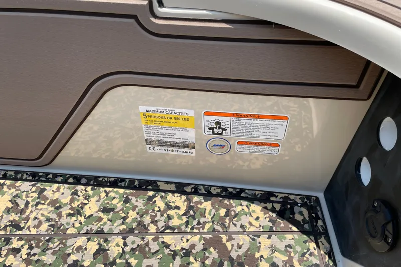Slide: The Image of Mako 18 Pro Skiff Backwater Edition 2026, capacity label and warning stickers on camouflage flooring. - 16