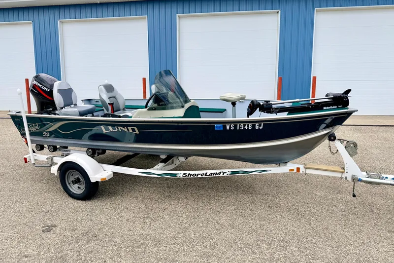 The Image of 2002 Lund 1650 Rebel SS fishing boat on ShoreLand'r trailer, parked outside blue building. - 1