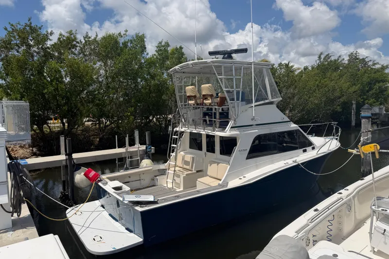 Slide: The Image of 2000 Cabo 35 Flybridge boat docked near lush greenery under a partly cloudy sky. - 26