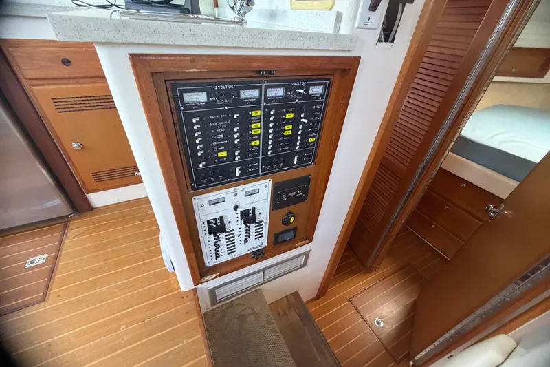 Slide: The Image of Electrical panel inside a 2000 Cabo 35 Flybridge boat, featuring wooden cabinetry and flooring. - 76