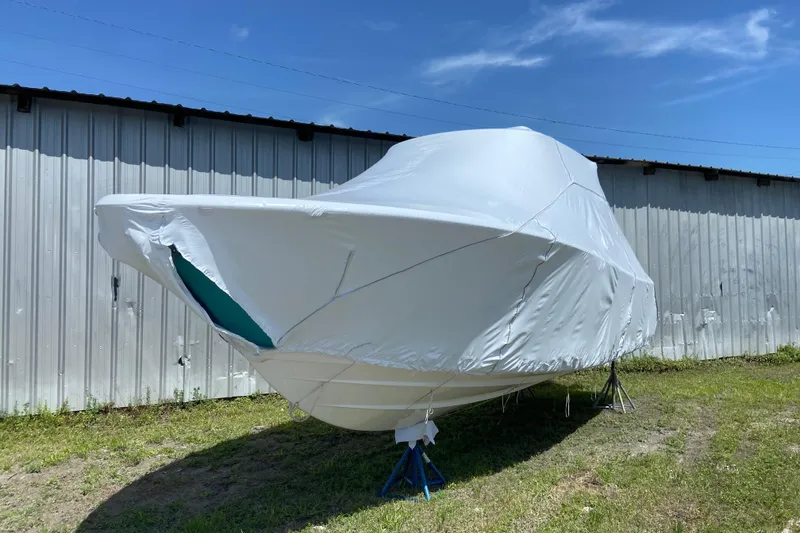 Slide: The Image of 2027 Sportsman Heritage 261 Center Console boat covered, stored outdoors near metal building. - 1